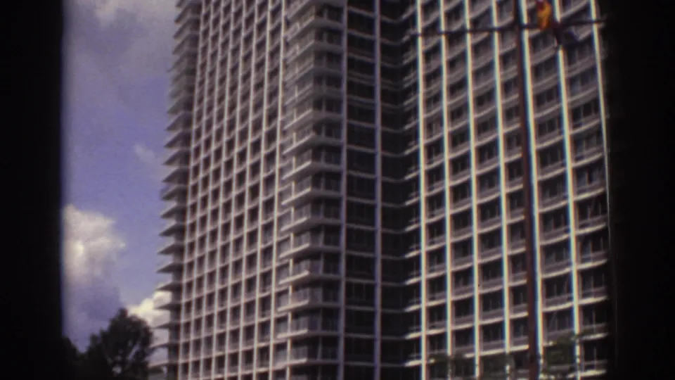 Large Cleveland hotel exterior in 1974, showing the gridded balcony facade, nearby trees, and bright sky in soft 8mm color.