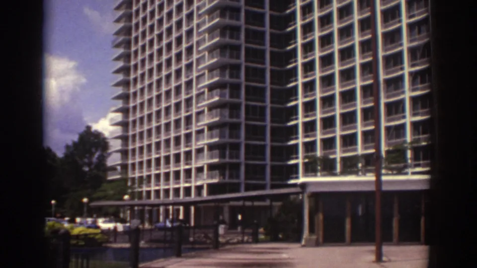 Street-level 1974 Cleveland view of the hotel base, entrance canopy, parked cars, trees, and the tall balcony grid above.