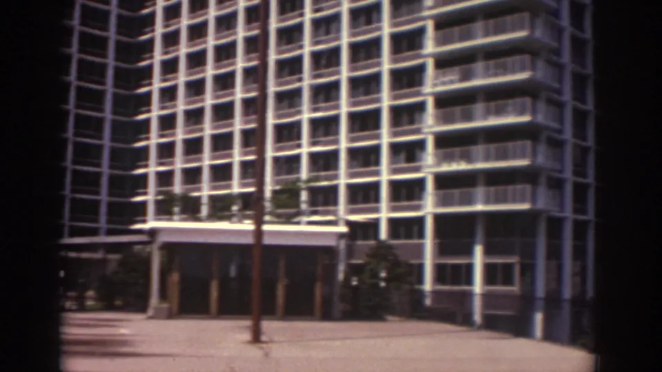 1974 Cleveland hotel exterior with the entrance canopy, flagpole, paved forecourt, trees, and gridded tower facade visible.