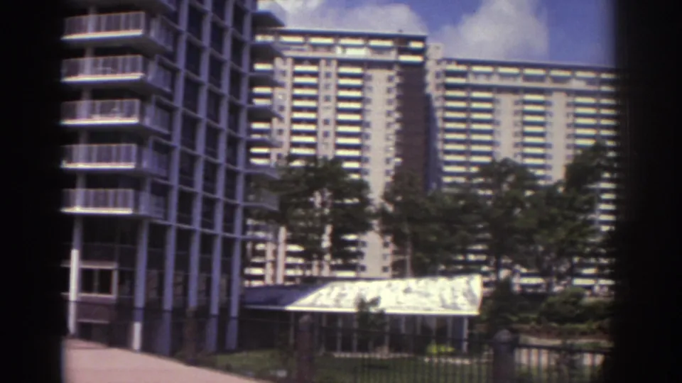 1974 Cleveland frame with apartment high-rises behind trees and a low covered structure in the foreground.