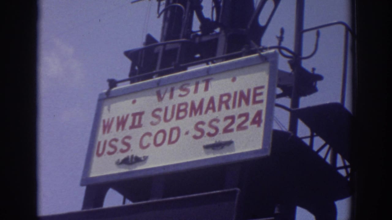 1974 Cleveland home-movie frame showing the USS Cod SS224 visitor sign mounted high on the submarine tower against sky.