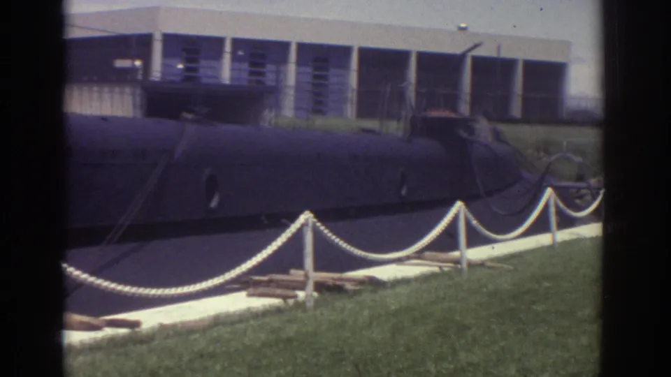 Wider 1974 Cleveland view of the black submarine display with white rope barriers, grass, and a low building behind it.