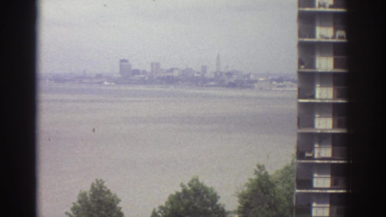Distant city skyline across wide water, partly framed by a high-rise building edge.