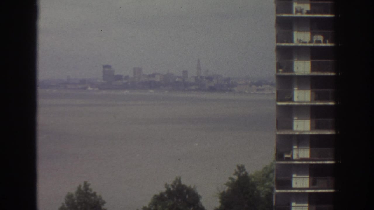 High-rise window view over water toward a hazy distant skyline and nearby building facade.