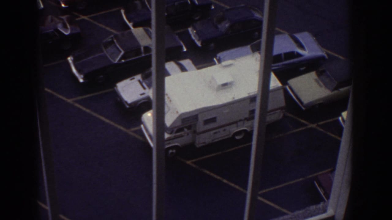 Overhead view from a window onto a parking lot with cars and a white camper van.