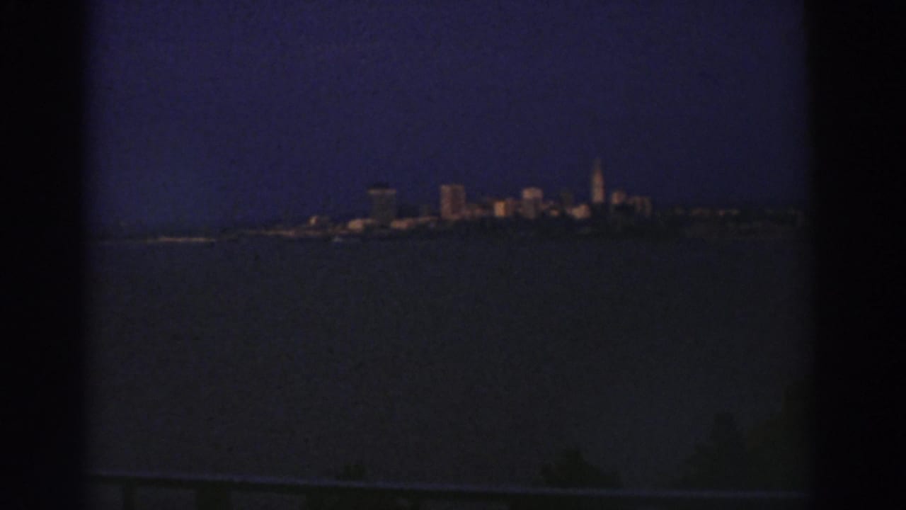 1974 Cleveland skyline likely seen across water at night, with low-light 8mm grain and dark frame edges.