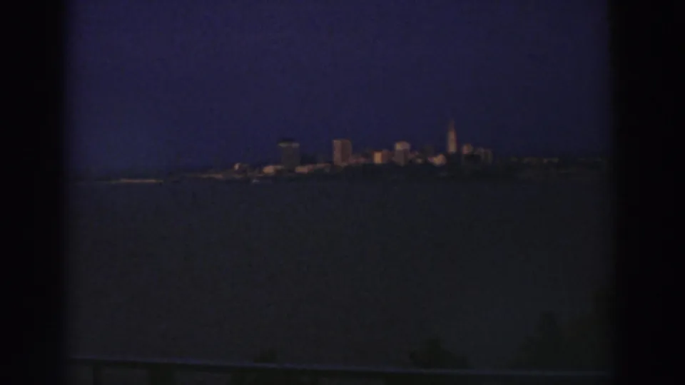 1974 Cleveland skyline likely seen across water at night, with low-light 8mm grain and dark frame edges.