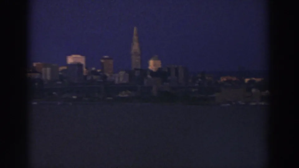 Closer 8mm view of the likely Cleveland skyline at night, with a prominent spire and waterfront foreground.