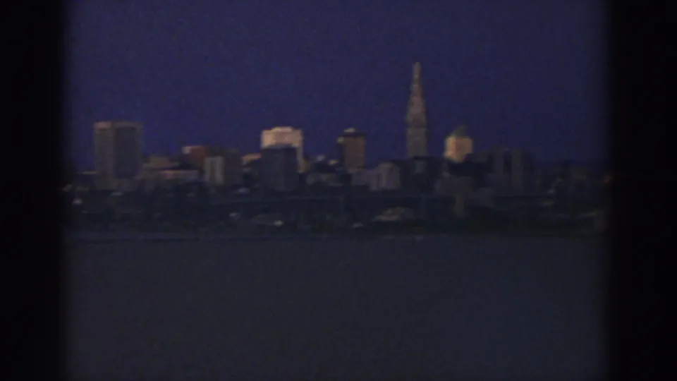 Likely Cleveland skyline across water in 1974, with a tall spire and soft low-light 8mm exposure.