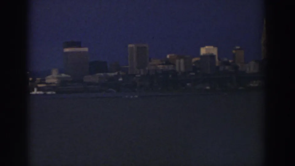 Cleveland downtown buildings appear across the water in a soft, grainy 8mm frame from 1974.