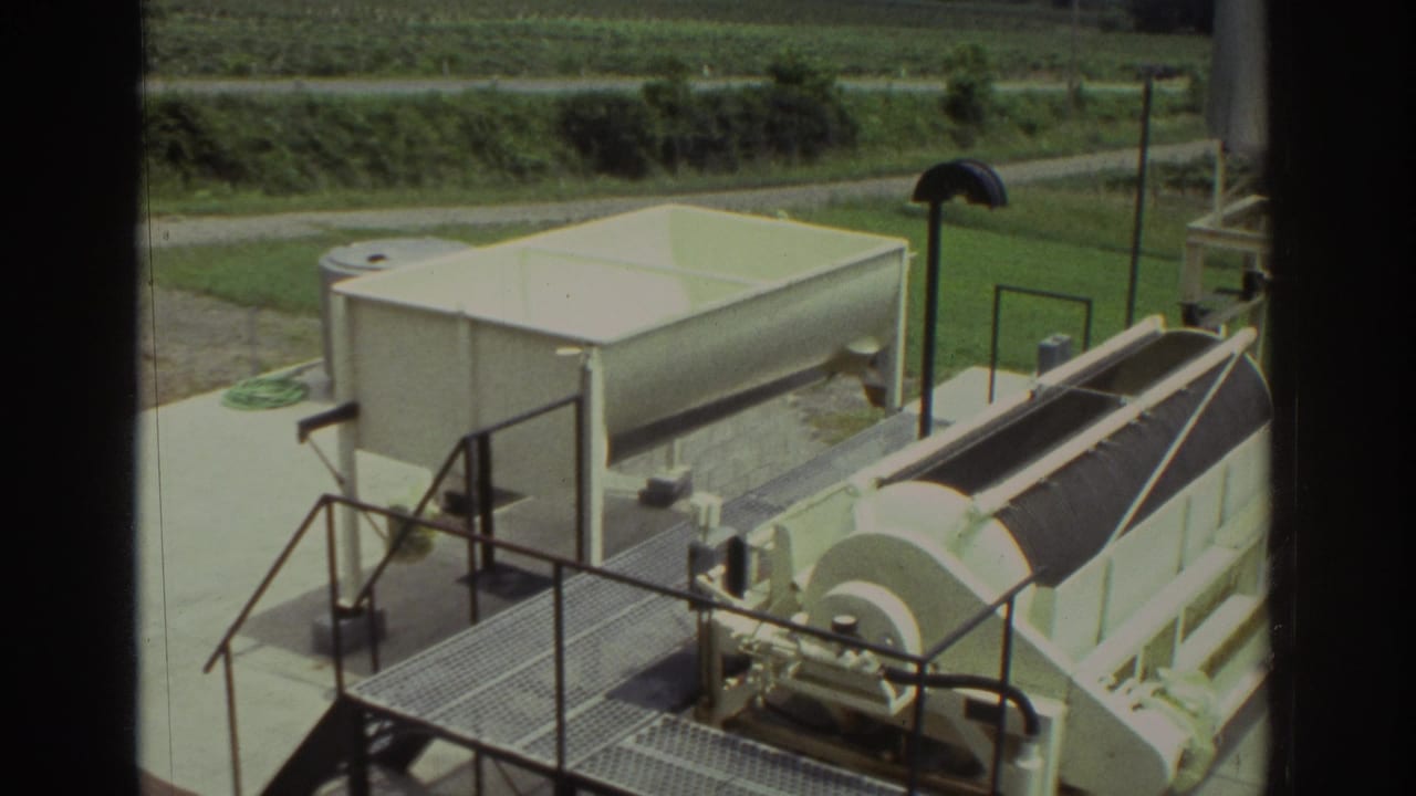 1974 Cleveland-area 8mm frame showing a white tank and covered drum equipment on a metal platform with countryside behind.