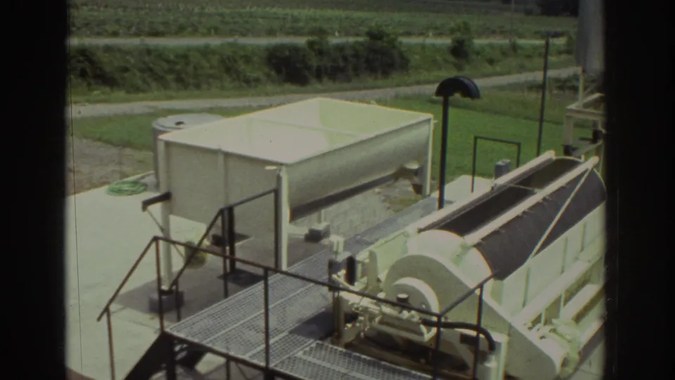 1974 Cleveland-area 8mm frame showing a white tank and covered drum equipment on a metal platform with countryside behind.