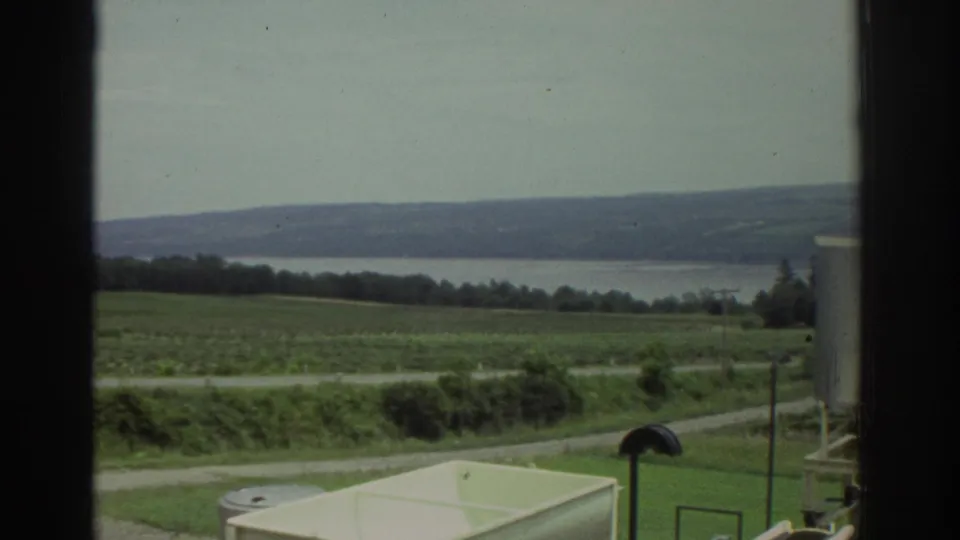 Cleveland-area 1974 8mm frame with dark window bars, green fields, a road, distant water, and partial tank equipment.