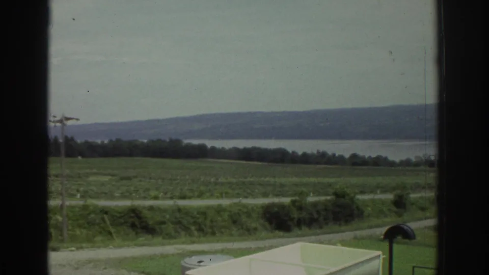 1974 8mm view near Cleveland showing open fields, a utility pole, distant water and hills, and part of a pale tank below.
