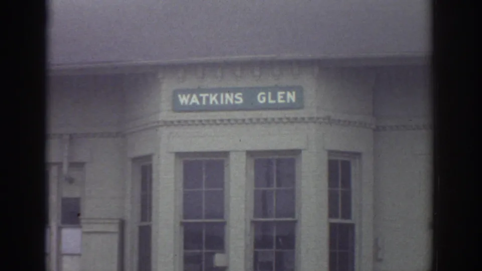A pale building facade with multi-pane windows is filmed below a green Watkins Glen sign, likely marking the travel stop shown in the clip.