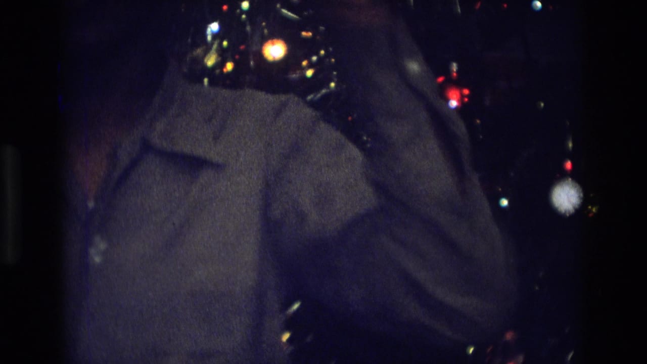 1975 Atlanta home-movie frame showing a partial silhouetted figure beside a decorated Christmas tree in low light.