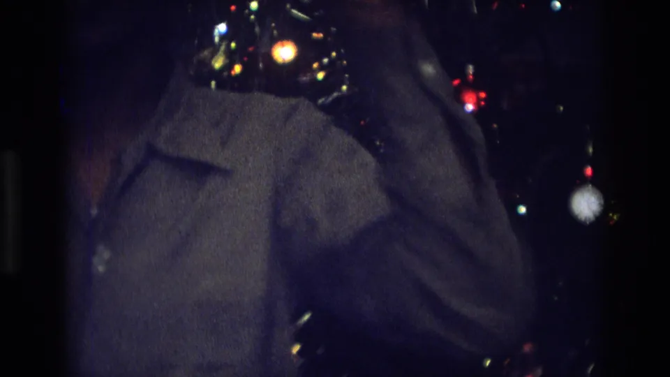 1975 Atlanta home-movie frame showing a partial silhouetted figure beside a decorated Christmas tree in low light.