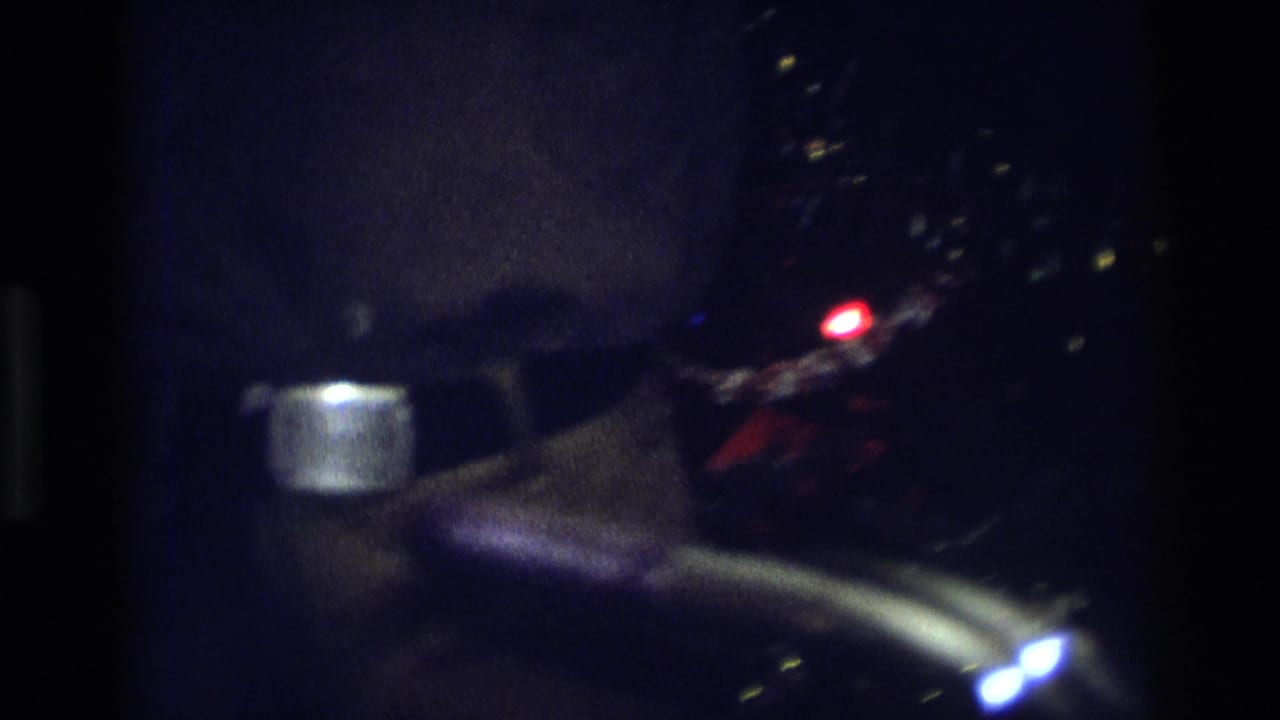 Dark 8mm frame from the 1975 Atlanta holiday interior, with tree lights and a partial figure visible in soft focus.
