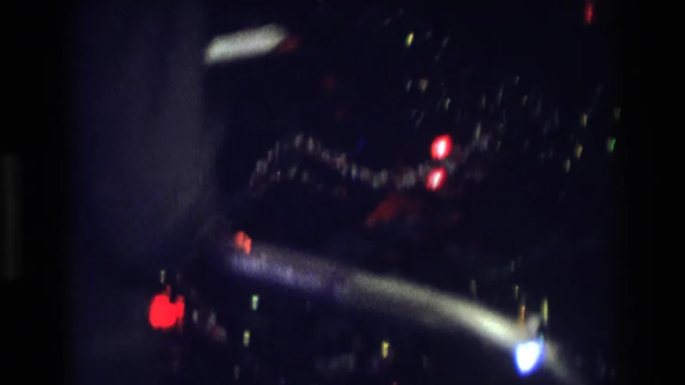 Final 1975 Atlanta home-movie frame with glowing Christmas lights, dark interior space, and a partial human silhouette.