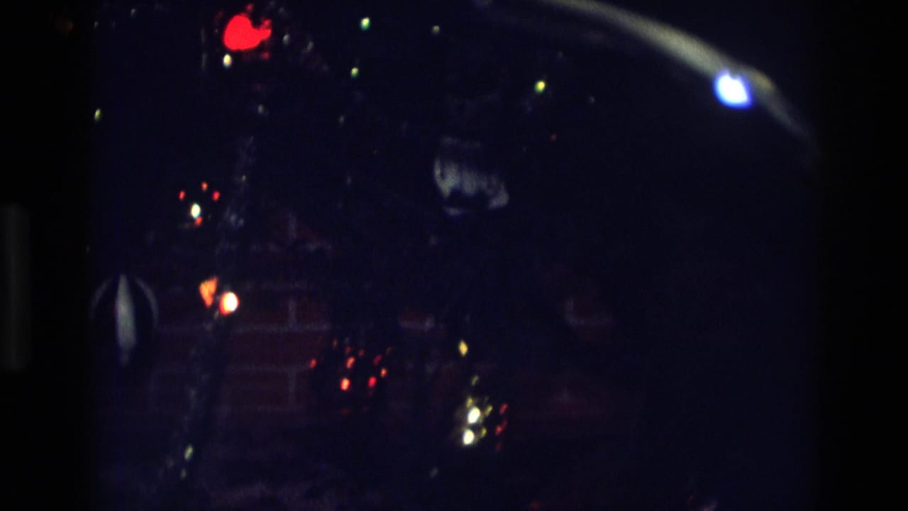 Low-light 1975 Atlanta home-movie frame showing colored lights and a dark rounded object against an interior brick wall.