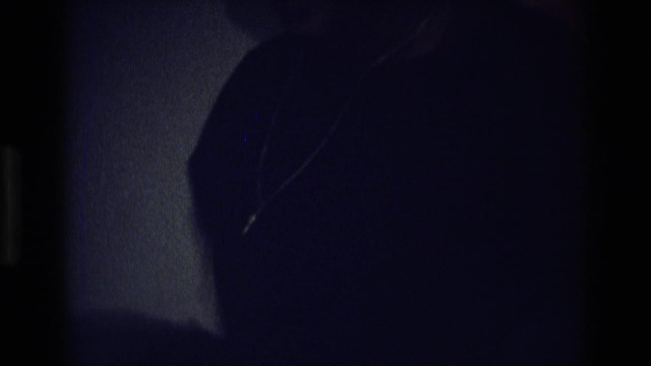 Dark 1975 Atlanta frame with a partially visible woman wearing a cross necklace inside a low-lit private room.