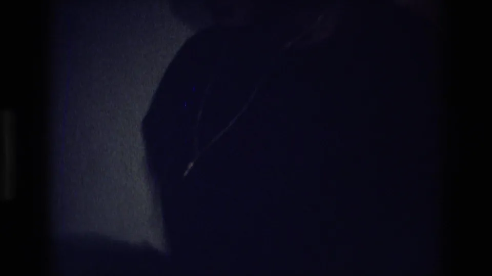 Dark 1975 Atlanta frame with a partially visible woman wearing a cross necklace inside a low-lit private room.