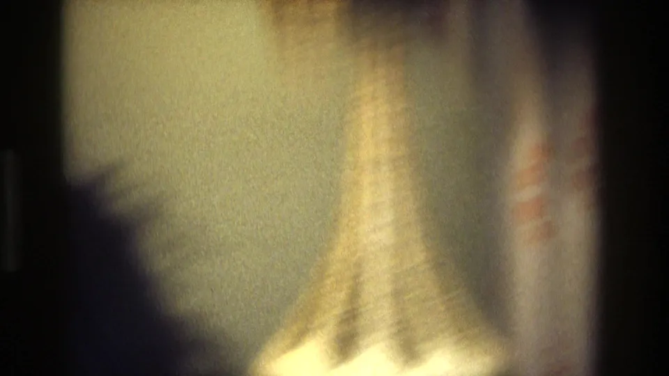 Soft, underexposed 1975 Atlanta home-movie frame with blurred shadowed figures and a pale interior surface.