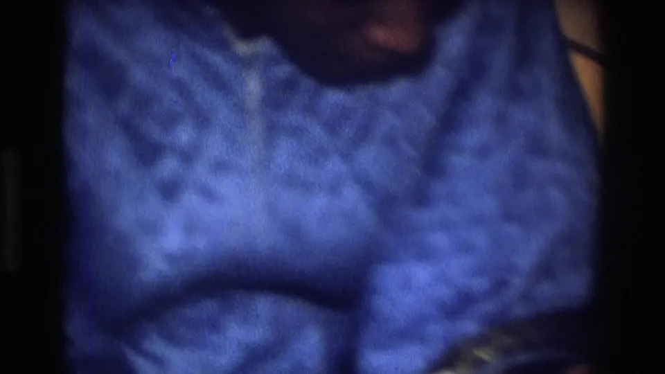 1975 Atlanta home-movie frame showing blue patterned clothing and a dark, partially visible figure in a dim interior.