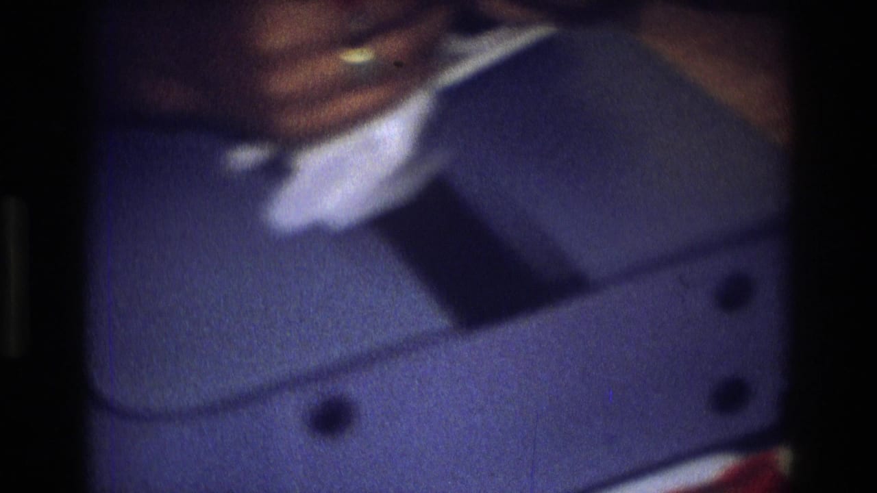 The frame shows a child seated indoors in Atlanta, with hands near a small blue suitcase on a sofa.