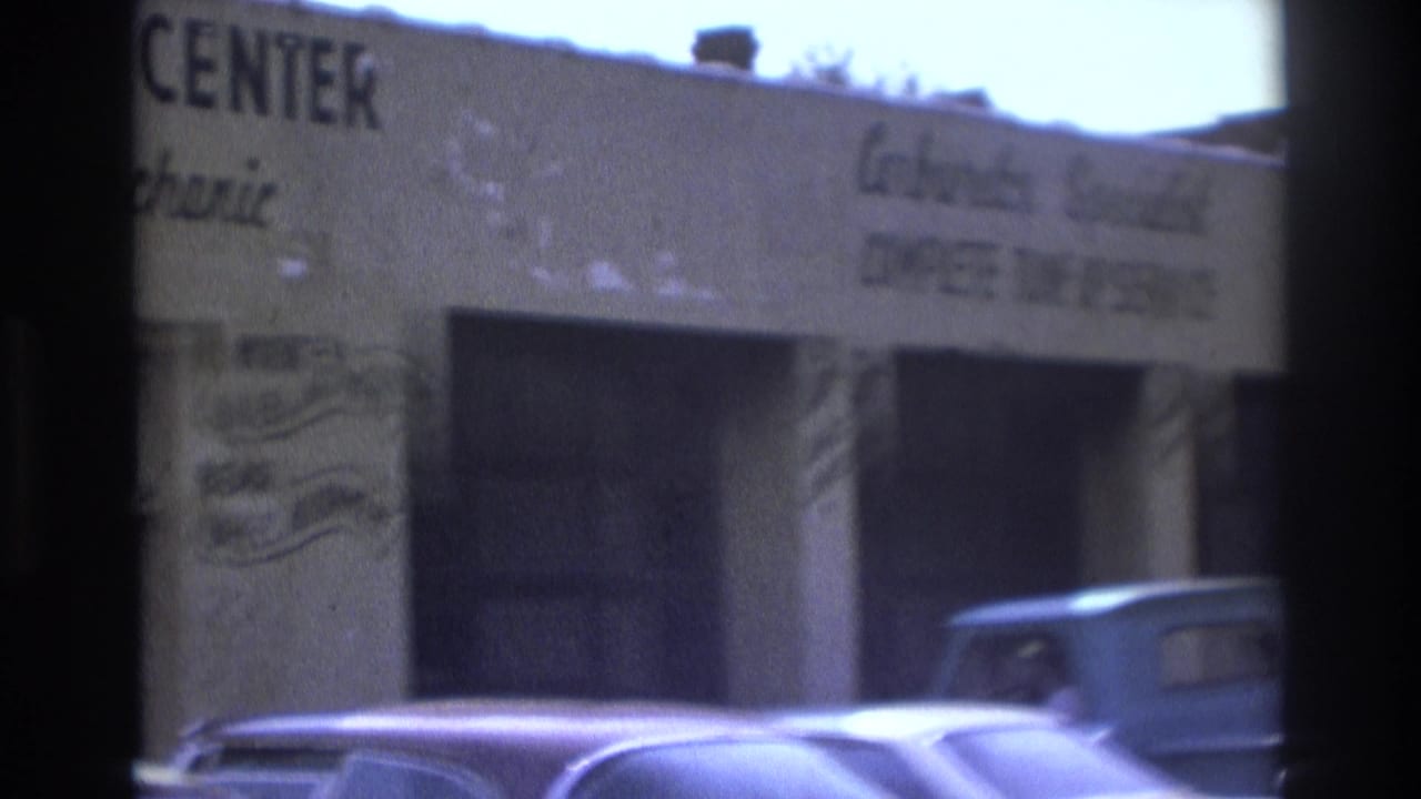 White building with tune-up center signage and older cars parked along the curb.
