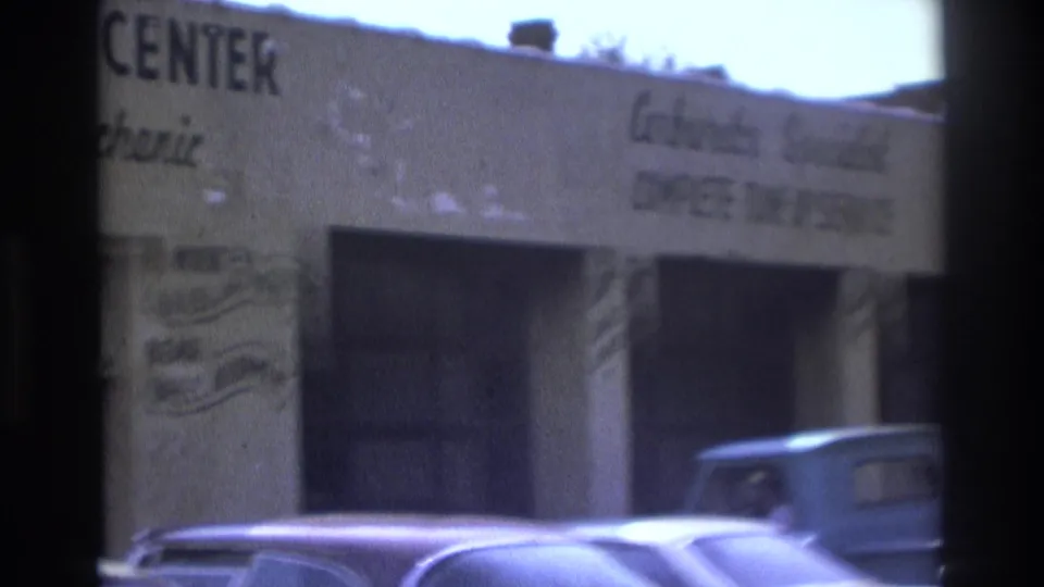Daytime 1975 Atlanta street view of a white auto-service building with tune-up signage and older vehicles at the curb.