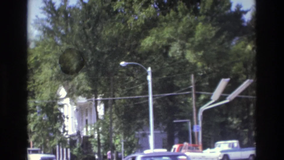 Atlanta-area drive-by view with trees, roadside buildings, parked vehicles, streetlights, and visible 8mm frame edges.