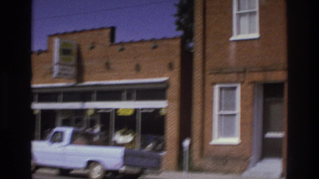 1975 Atlanta home-movie frame showing a pale pickup truck by a brick storefront and neighboring building facades.