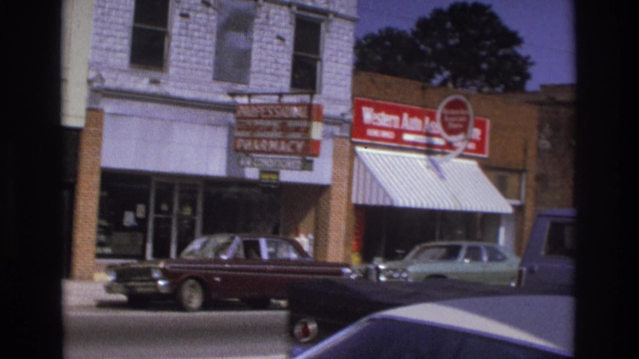 1975 Atlanta street view with storefronts, a Western Auto sign, parked cars, and passing traffic on a commercial block.