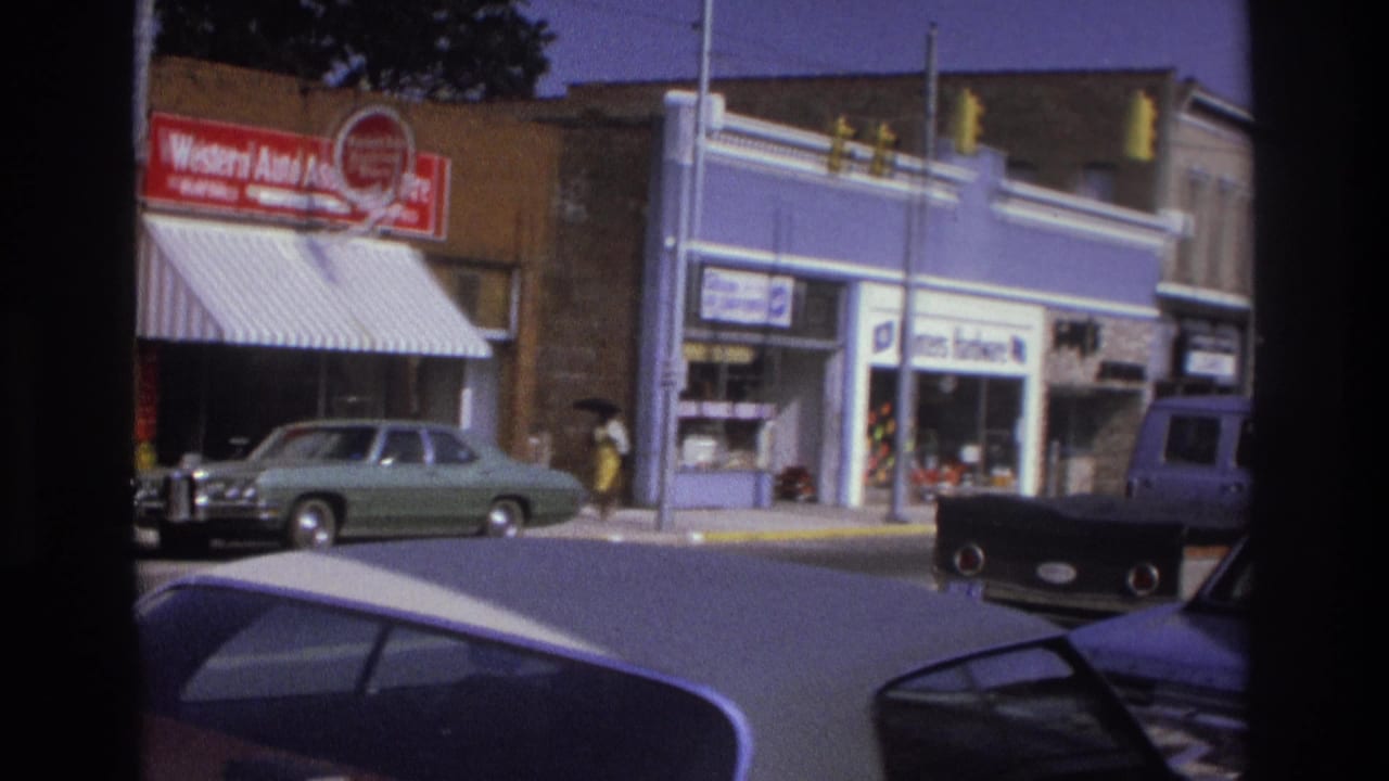 1975 Atlanta corner view showing Western Auto signage, a light green car, traffic lights, and a pedestrian near storefronts.