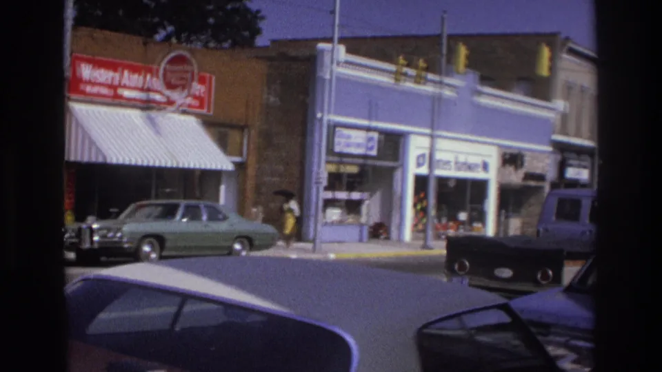 1975 Atlanta corner view showing Western Auto signage, a light green car, traffic lights, and a pedestrian near storefronts.