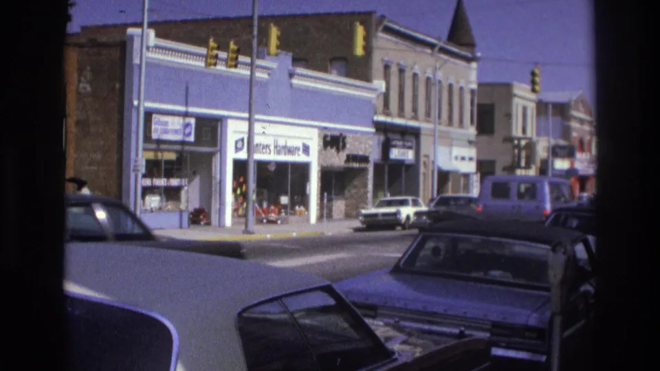 1975 Atlanta street scene with hardware and retail storefronts, hanging traffic lights, parked cars, and foreground automobiles.