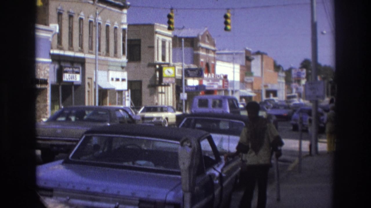 1975 Atlanta street view with classic cars, storefront signs, traffic signals, and a person standing near an open car door.