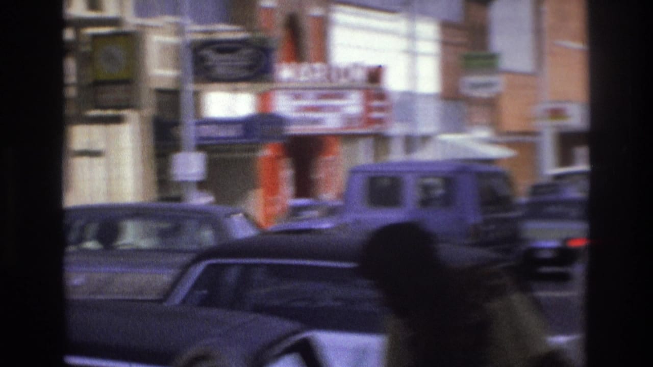 Blurred street view with classic cars, storefronts, and a pedestrian silhouette in the foreground.
