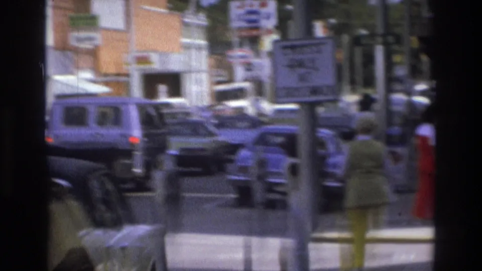 1975 Atlanta street scene with traffic, parked cars, a roadside sign, storefronts, and pedestrians on the sidewalk.