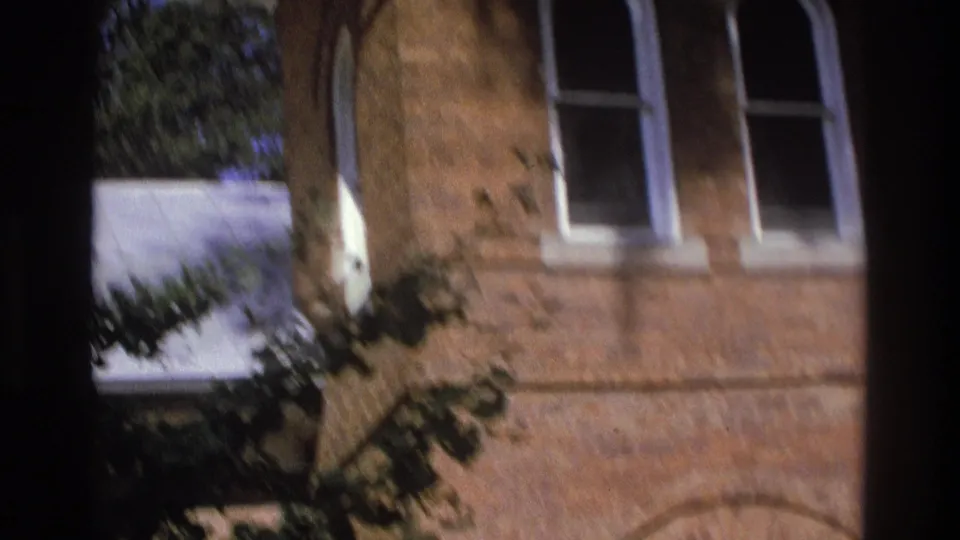 1975 Atlanta 8mm frame showing a brick building with arched masonry detail, windows, and leafy branches.