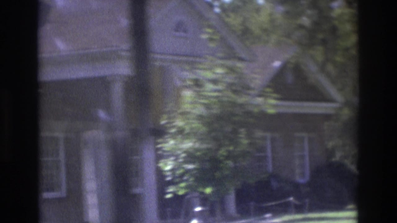 House facade with porch columns, trees, and a parked car near the curb.