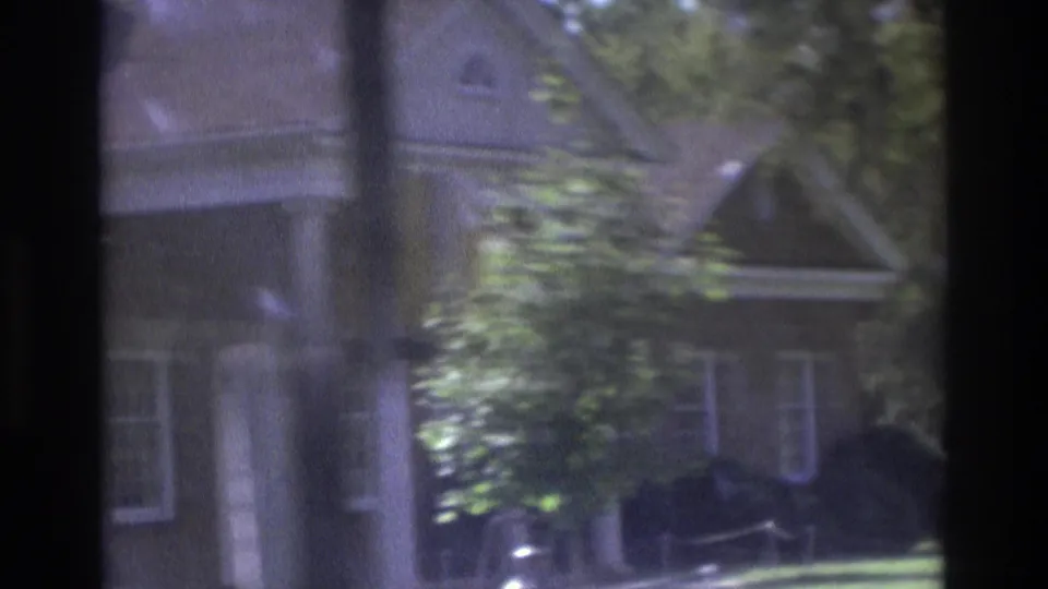 Soft 8mm view of a residential house in Atlanta, Georgia, with porch columns, trees, and a partially visible parked car.