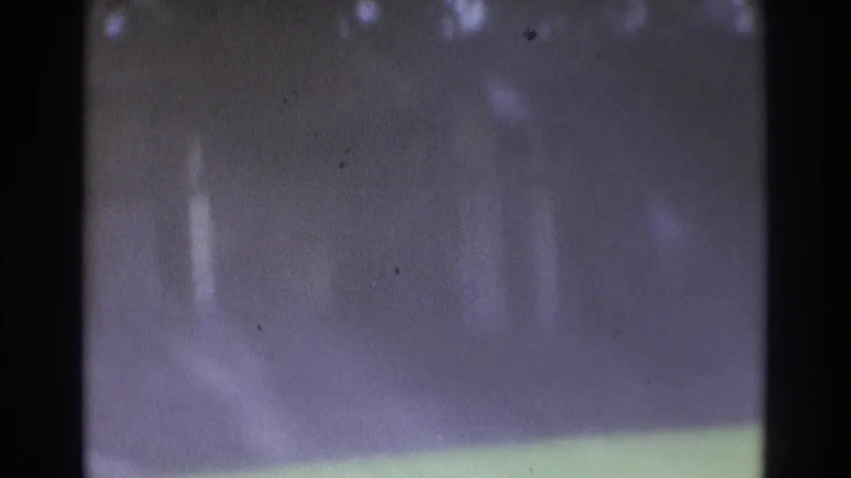 Heavily softened 8mm frame from the Atlanta clip showing a house exterior, lawn, and dark foreground obstruction.