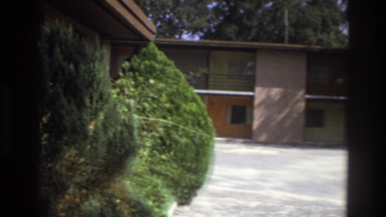 Atlanta 1975 frame showing a two-story motel building, trimmed shrubs, trees, and a bright paved parking lot.