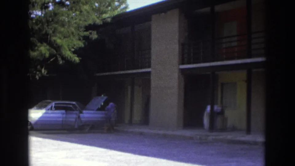 Atlanta 1975 frame showing a vintage car with its hood open near a motel room walkway and shaded exterior.