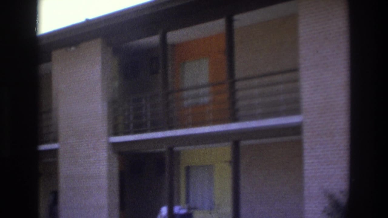 1975 Atlanta frame focused on upper-level apartment balconies, brick columns, metal railings, and orange door accents.