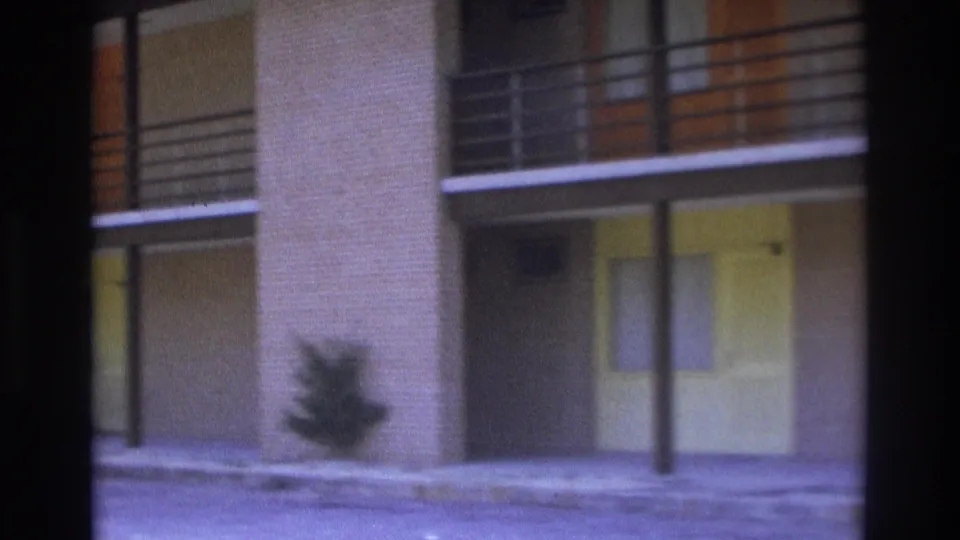 1975 Atlanta home-movie frame showing the apartment facade, upper railings, ground-floor doors, posts, shrubs, and soft film grain.