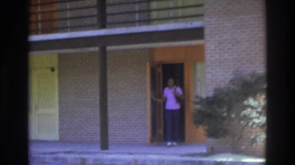 1975 Atlanta 8mm frame showing the woman more clearly in the orange-trimmed doorway of a brick apartment exterior.
