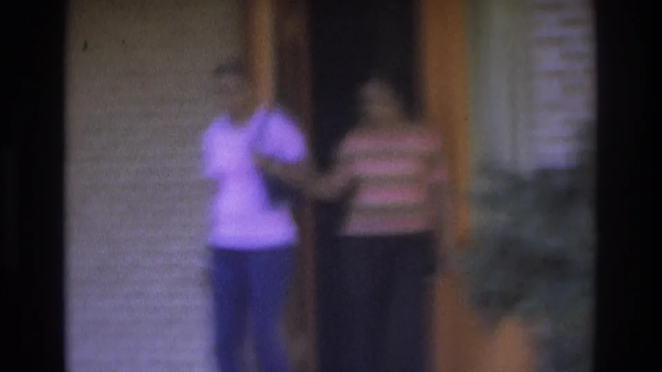 1975 Atlanta frame of two women leaving a brick house through an orange wooden door, with one gesturing toward the camera.